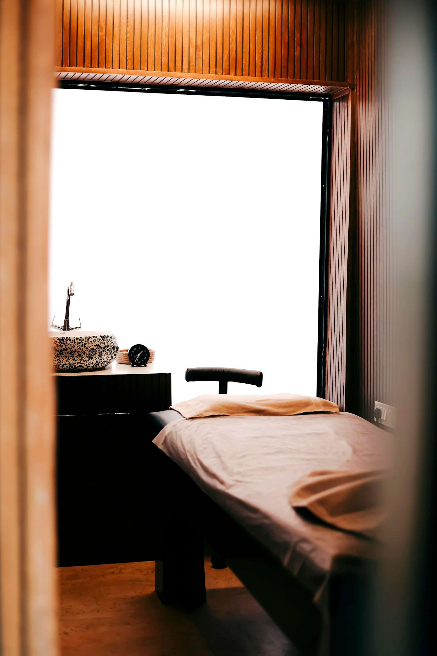 A massage table with a beige sheet by a window, next to a plant