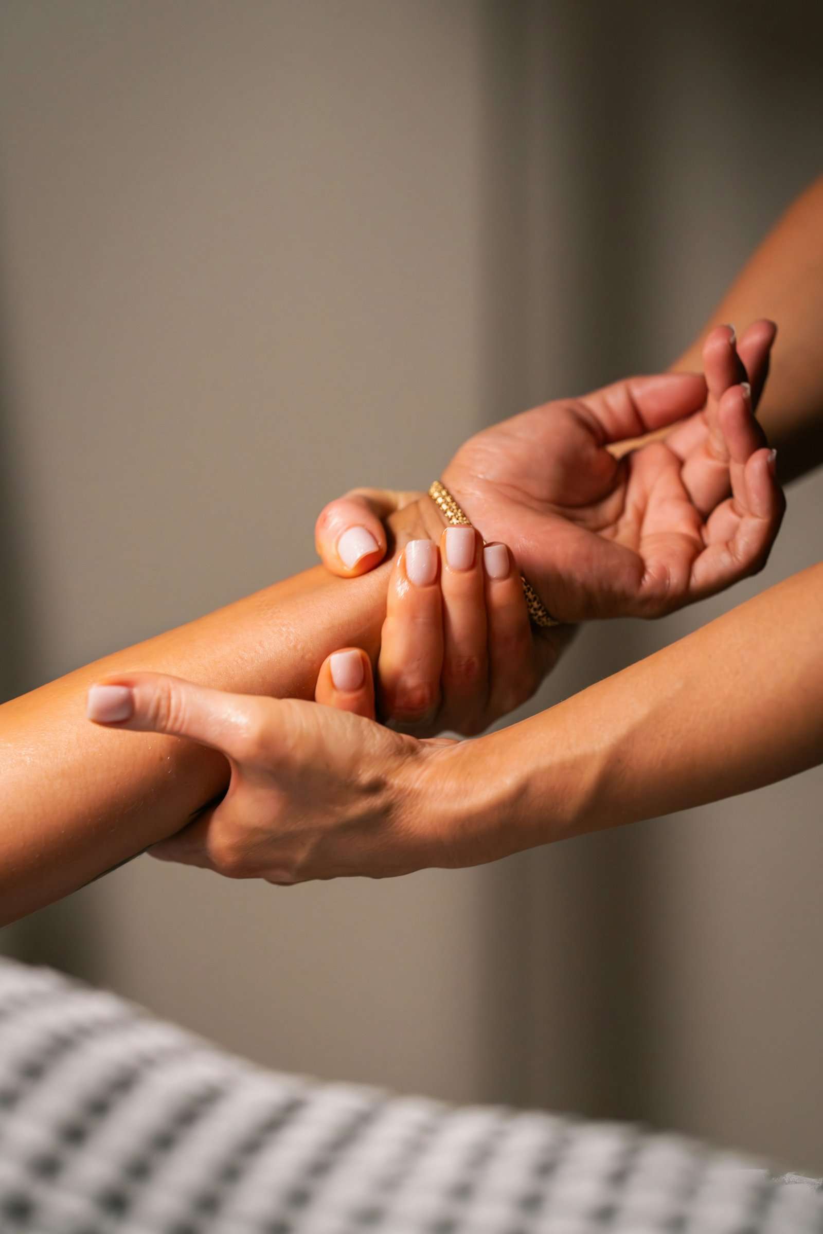 Two hands massaging a forearm with oil, soft light and a linen towel on the treatment table